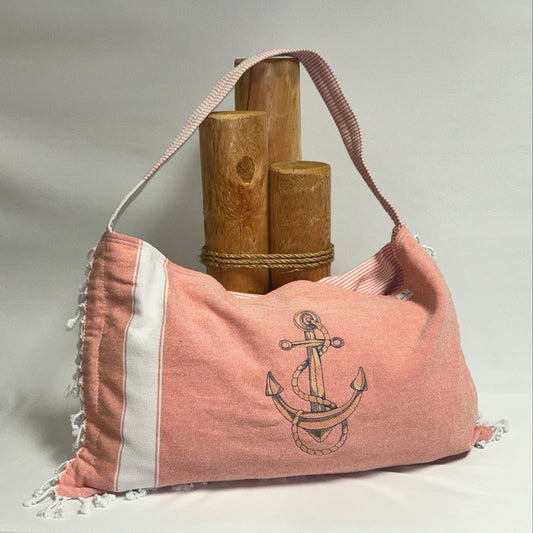 A peach cotton shoulder bag with white stripes, fringed edges, and an embroidered anchor design, displayed on a white background with wooden props.