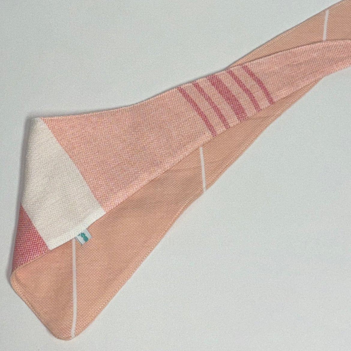 A folded pink and white striped fabric bandana or scarf with white stitching, laid flat on a light gray background.