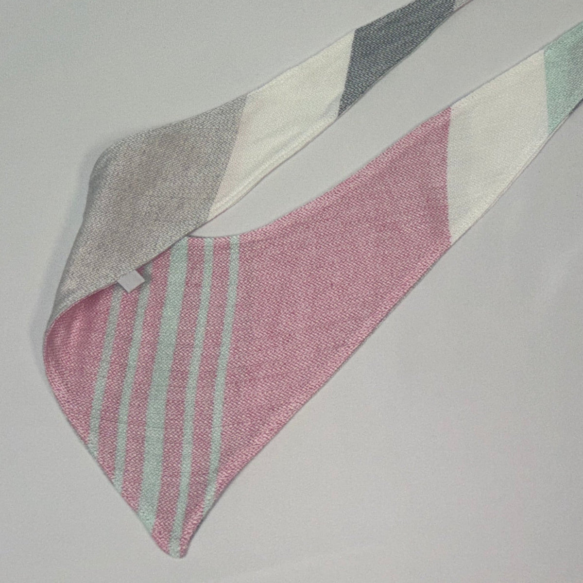 A triangular woven bandana or scarf in pink, white, gray, and mint green, folded to show its striped pattern and texture on a light gray background.