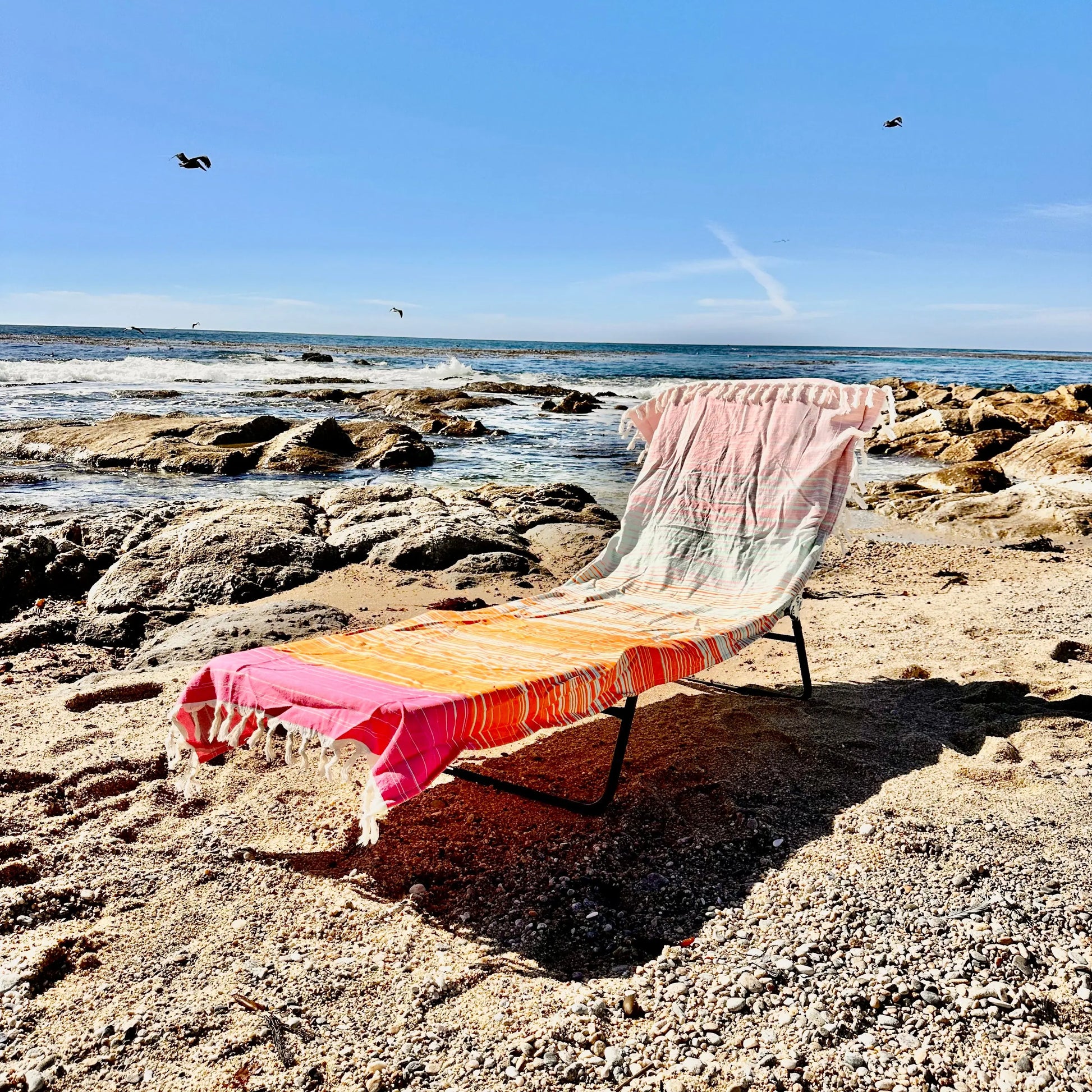 Beach chair with colorful towel on a rocky beach with ocean and sky in the background