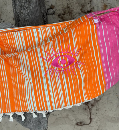 Orange and Pink striped bag with eye design hanging on a tree
