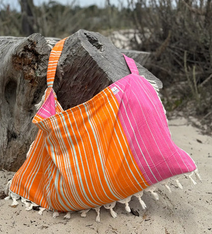Orange and pink striped bag on a sandy beach with driftwood in the background