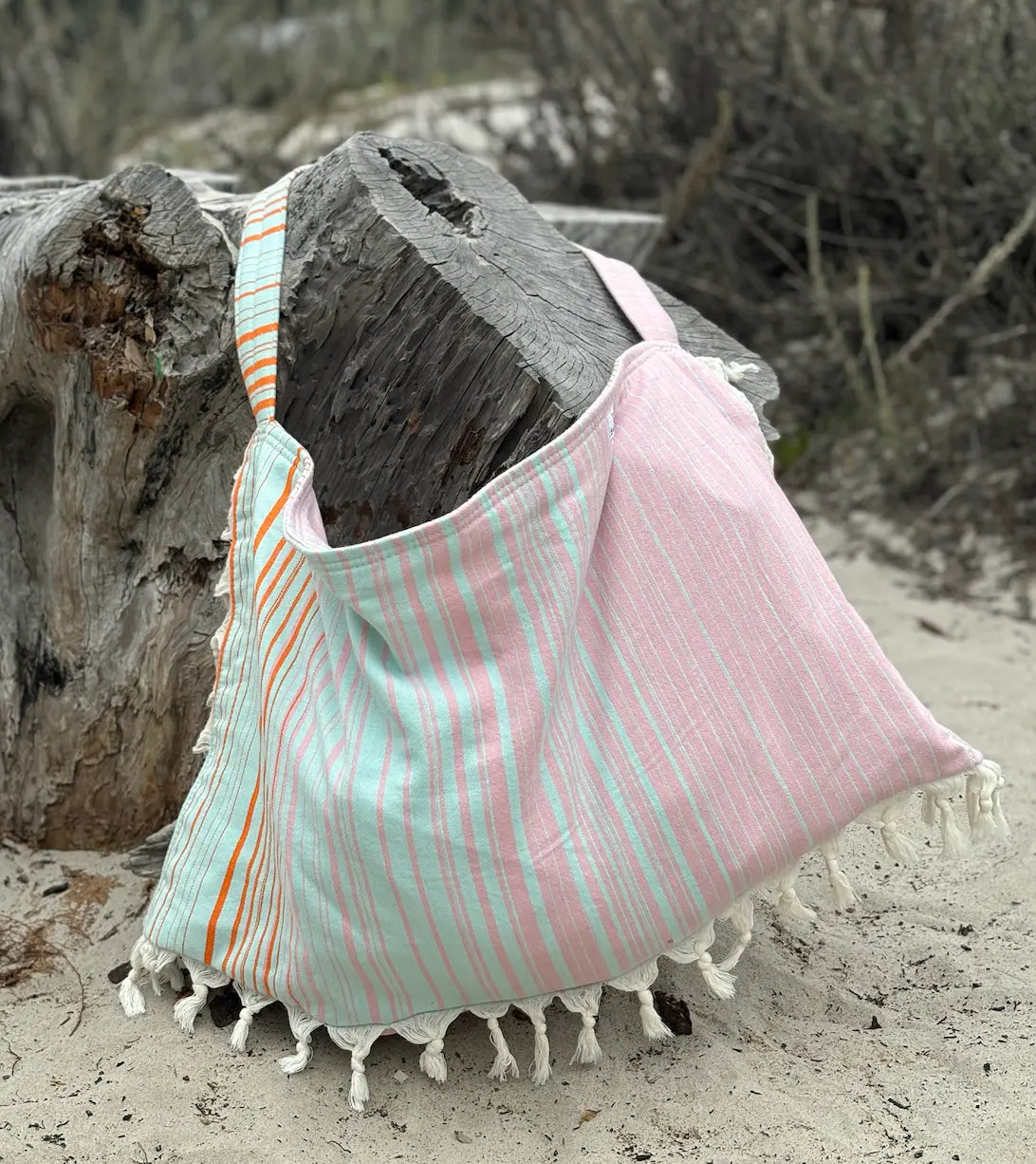 pink and aqua striped beach bag with tassels on a sandy background