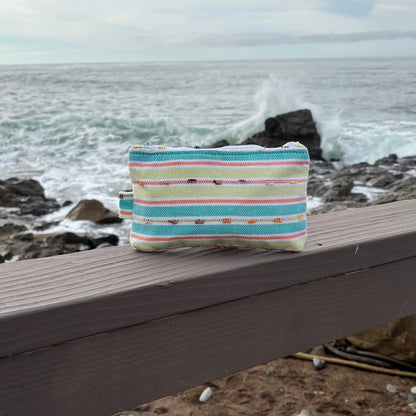 green Striped pouch on a wooden bench with ocean waves in the background
