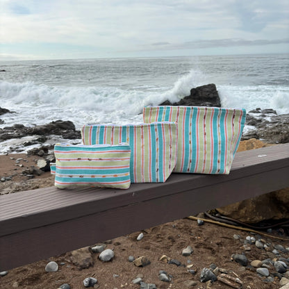 Striped bags on a wooden bench by the ocean with waves crashing in the background