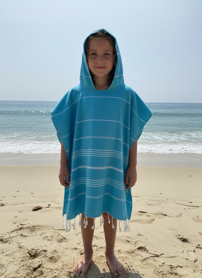 Child wearing a blue hooded towel poncho on a beach with ocean in the background