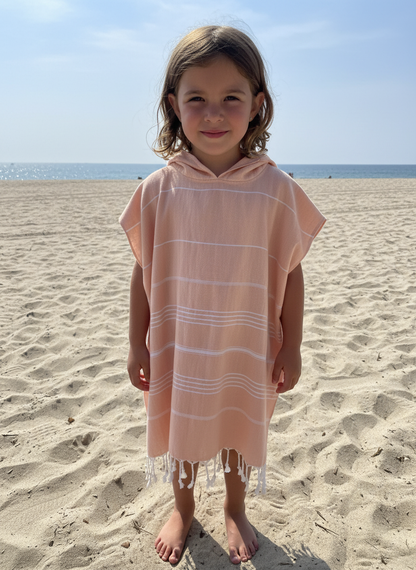 Child wearing a striped peach hooded  poncho on a sandy beach with ocean .