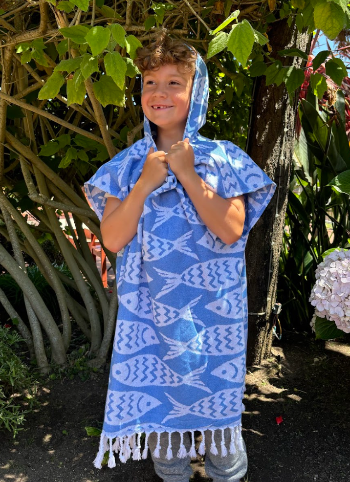 A child wearing a blue and white fish print hooded sun poncho tassel detailing, standing outdoors.