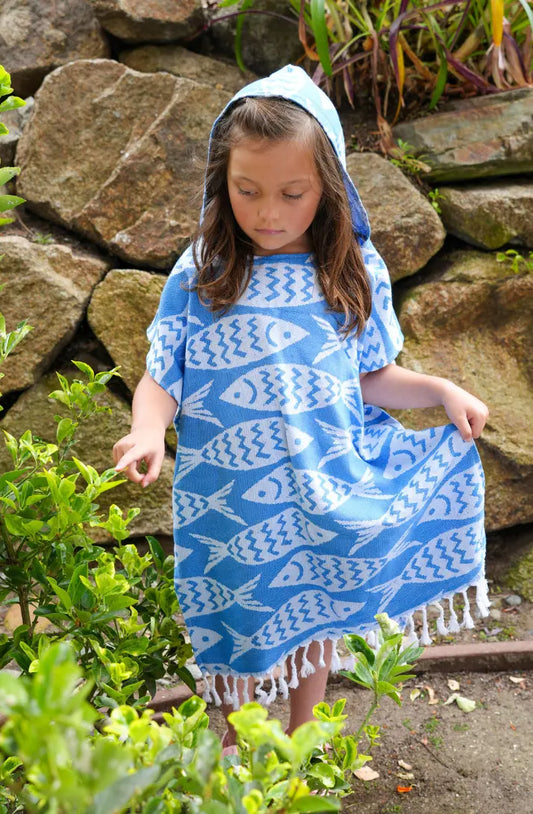 Child wearing a blue and white patterned hooded poncho standing in front of a stone wall.