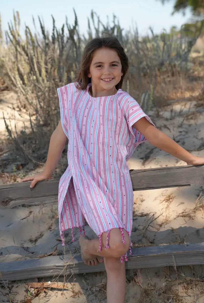 Young girl in a striped  poncho standing on a wooden platform with cacti in the background