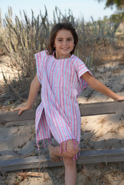 A child wearing a pink striped hooded sun poncho with tassel detailing, standing outdoors.