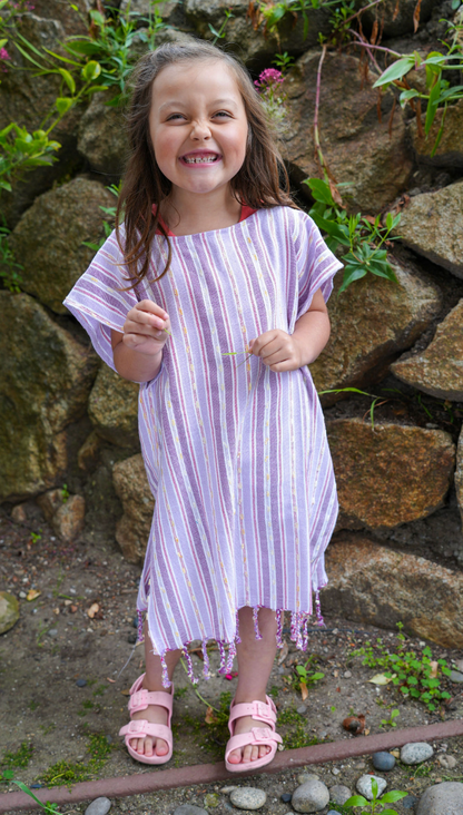 A child wearing a purple striped hooded sun poncho with tassel detailing, standing outdoors.