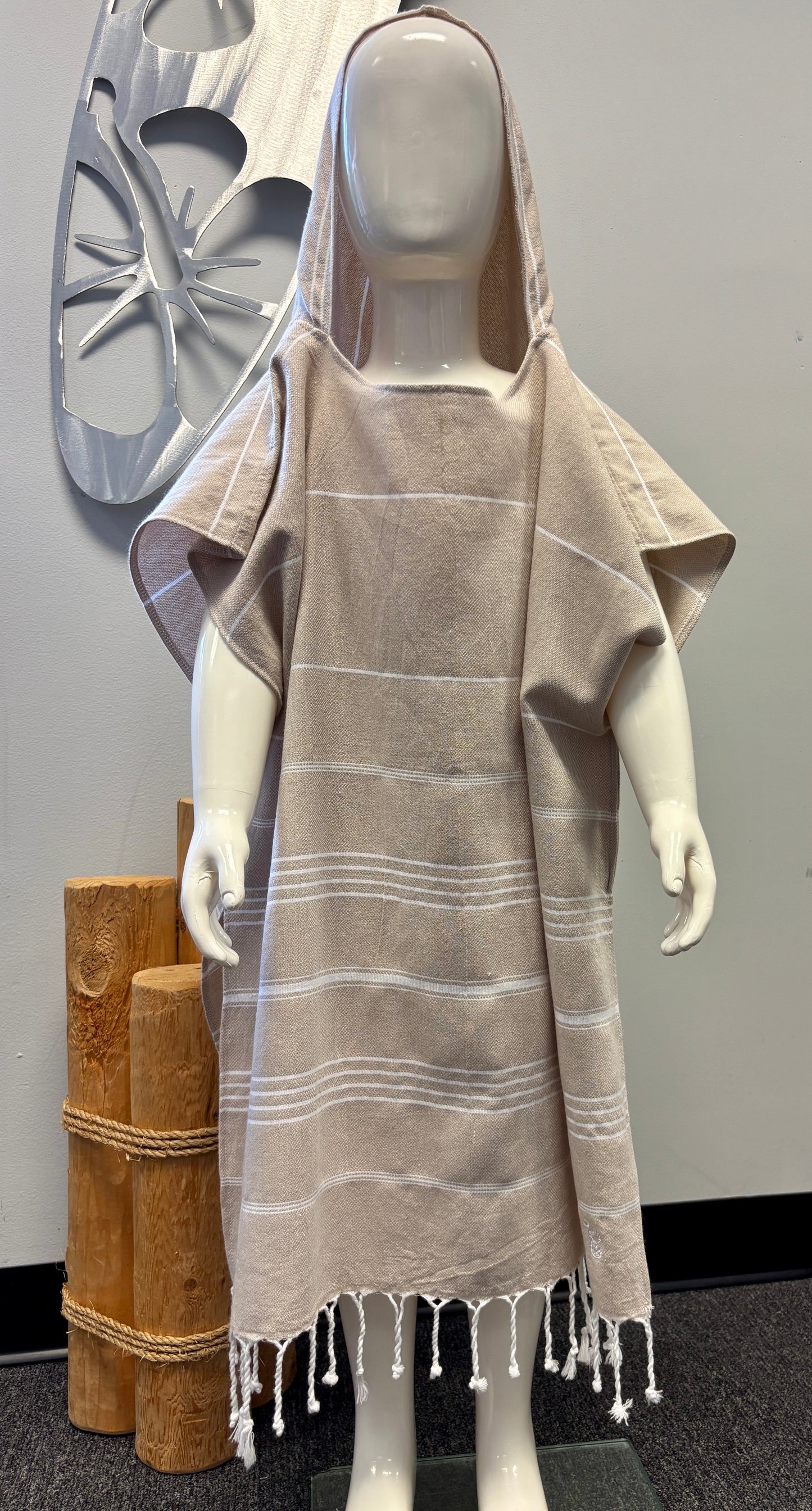A child mannequin wearing a tan striped hooded sun poncho with tassel detailing