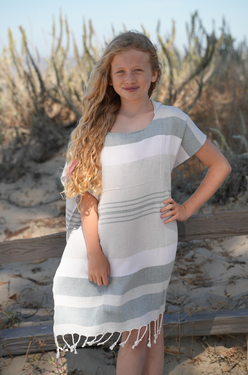 A child wearing a charcoal, grey and white striped hooded sun poncho with tassel detailing, standing outdoors.