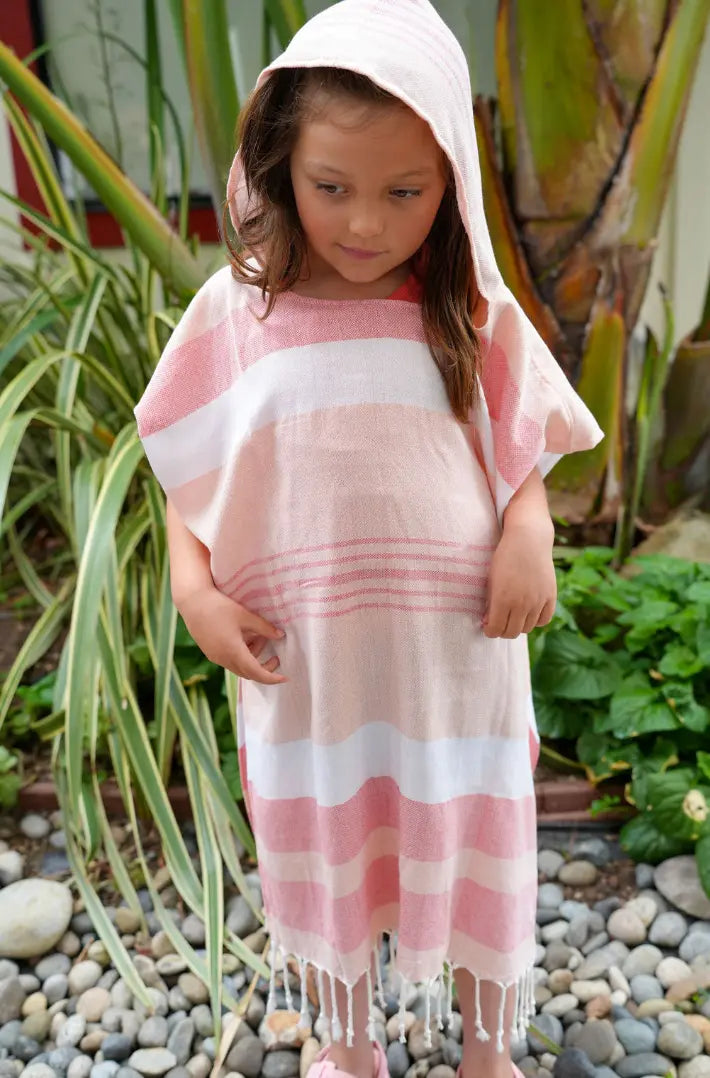 Child wearing a peach and white striped hooded poncho in a garden setting
