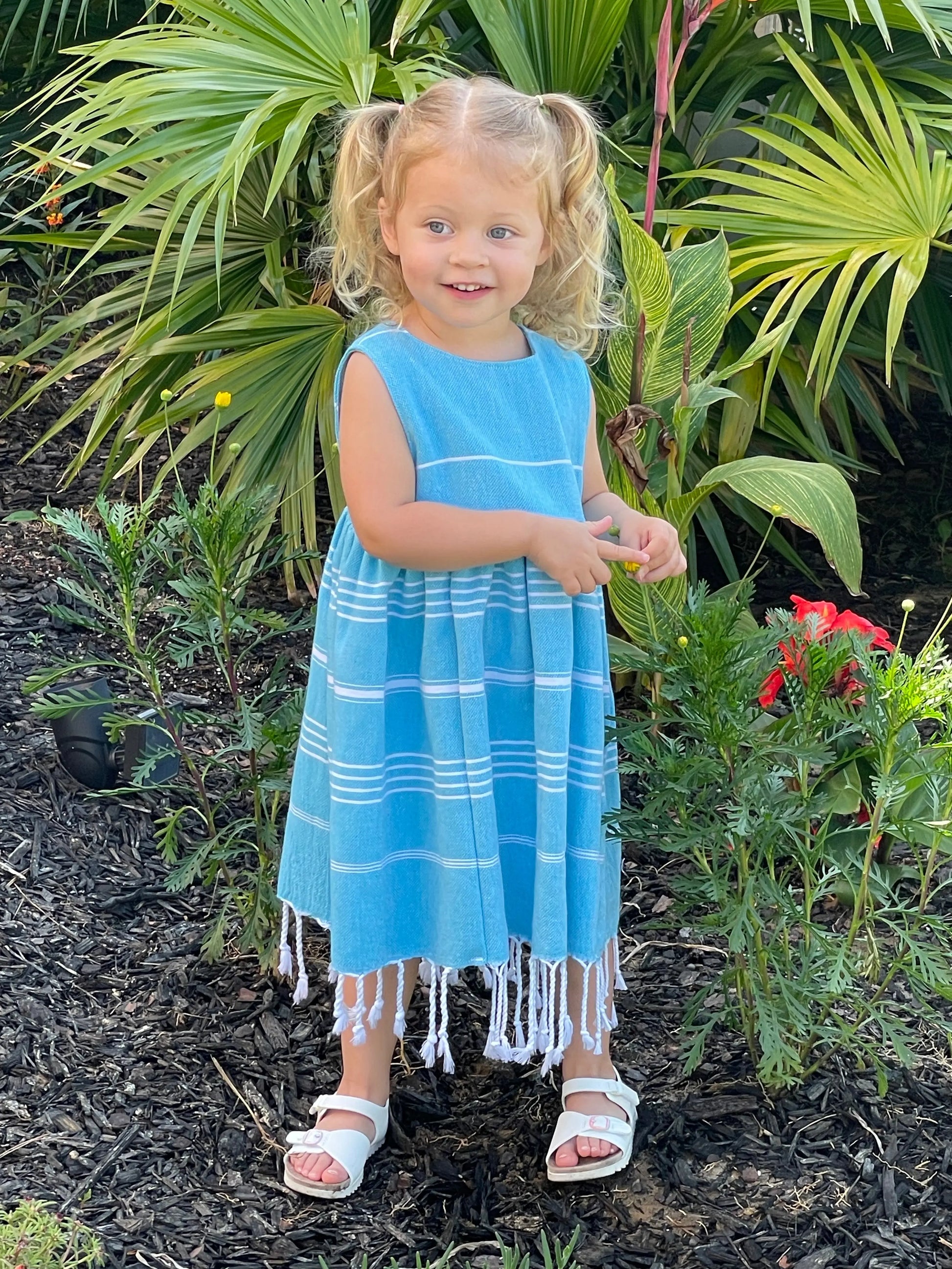 Child in a blue striped dress standing among green plants