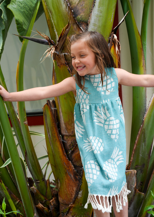 Young girl wearing a green pineapple print dress with tassels playing in large plants