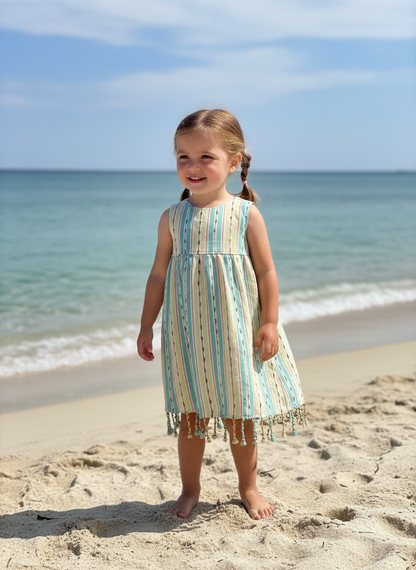 Young girl in a green striped dress standing on a beach with ocean in the background