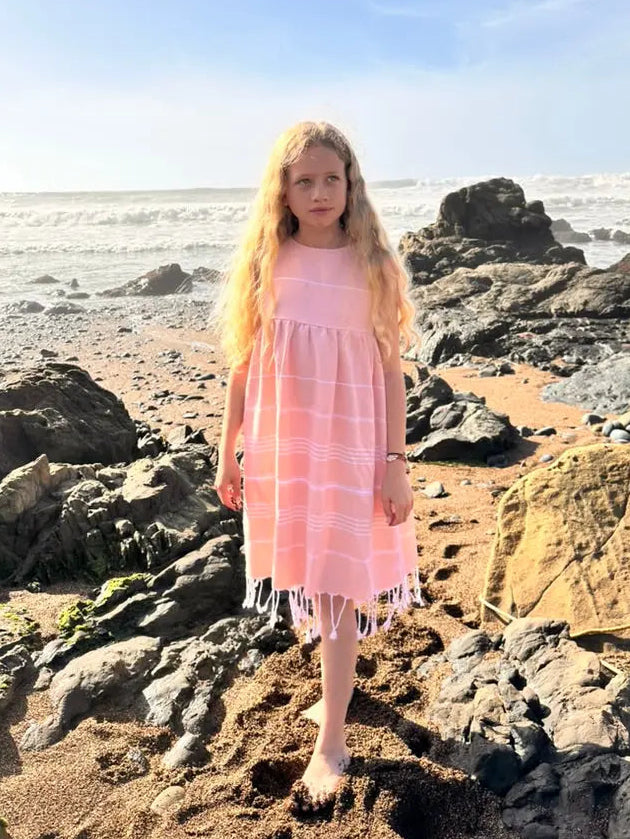 Young girl in a peach dress standing on rocky beach with ocean in the background