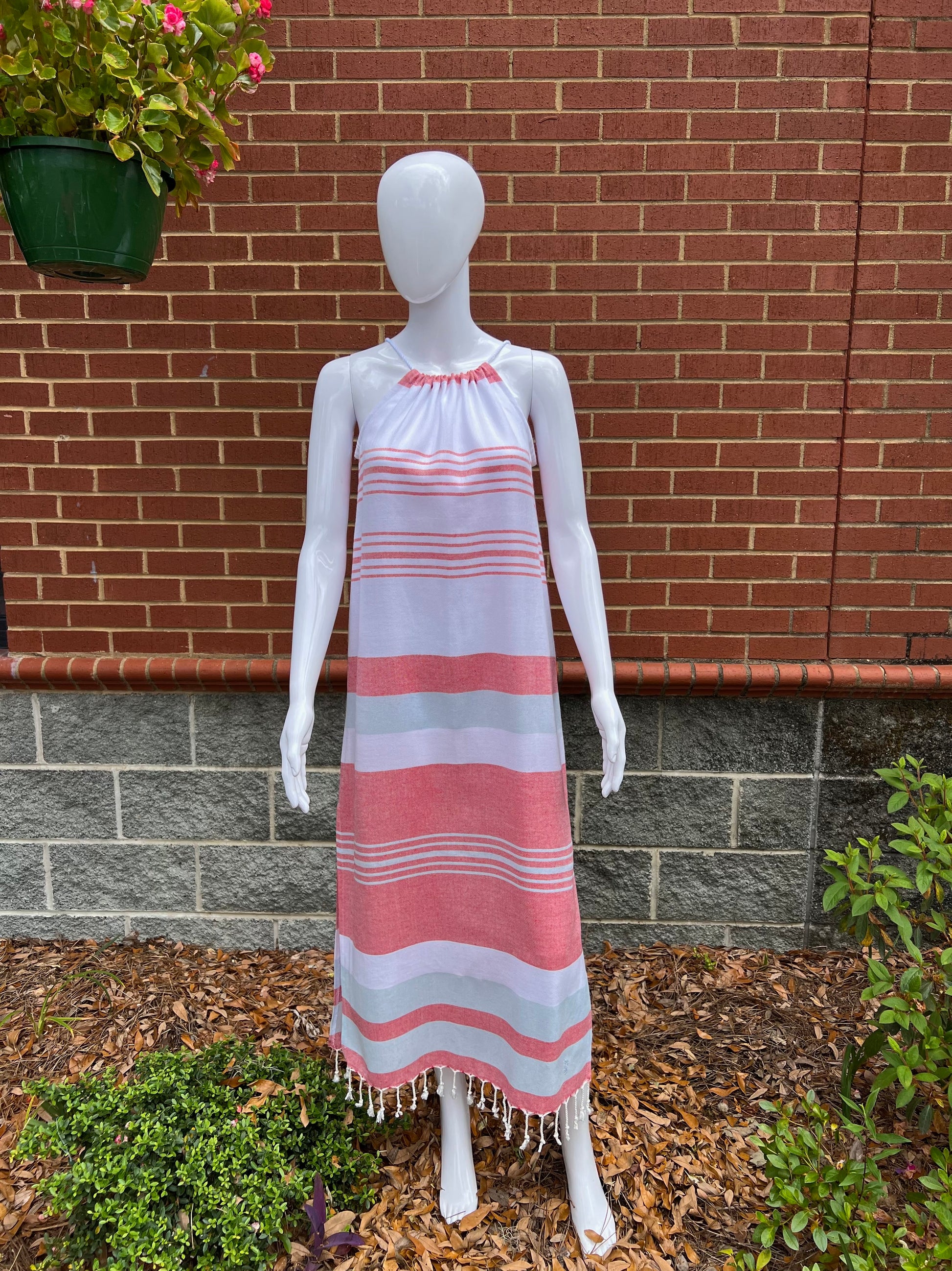 Mannequin wearing red, blue and white striped sleeveless maxi sundress with tassels in front of brick wall 