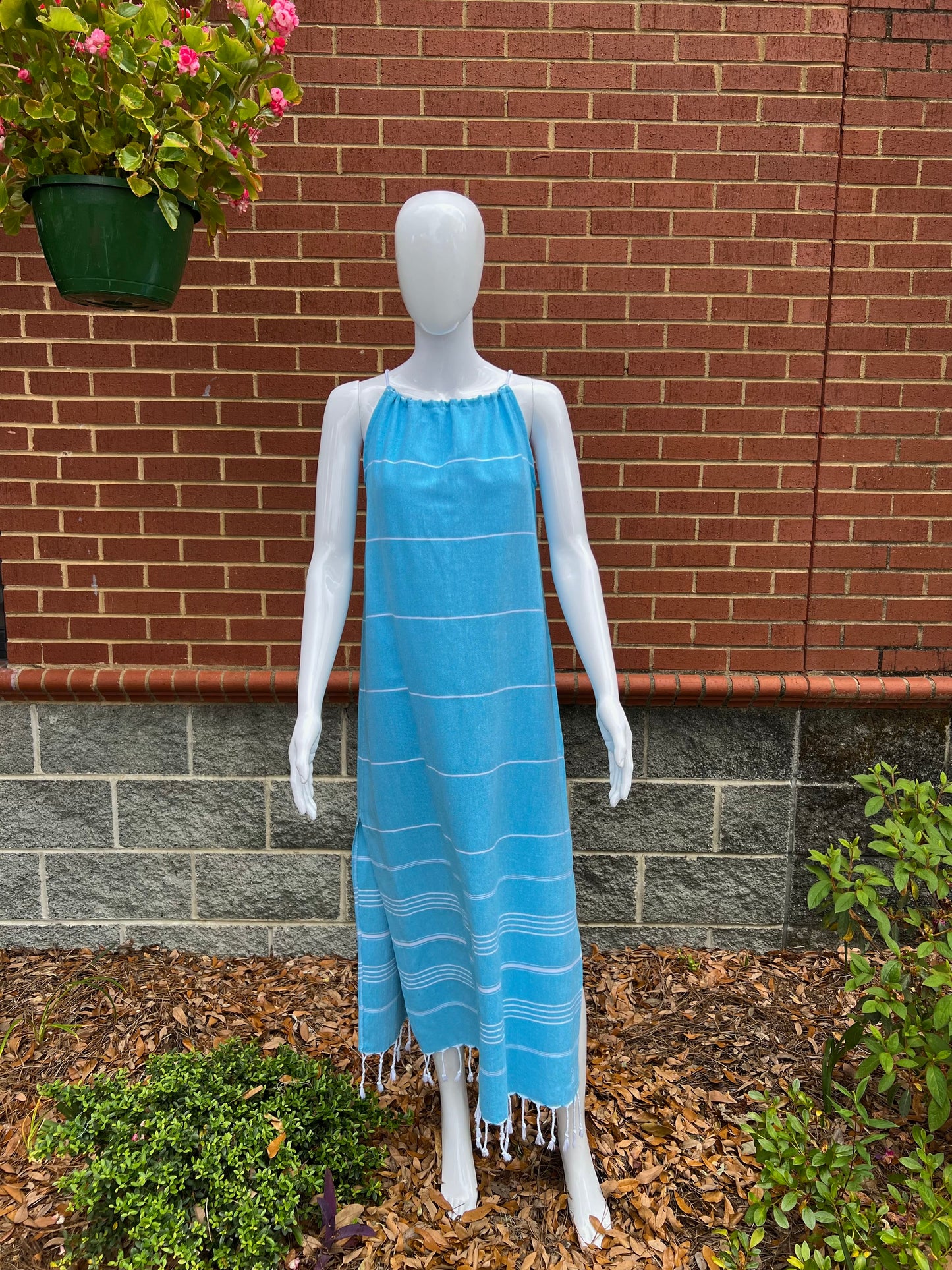 Mannequin wearing blue striped sleeveless maxi sundress with tassels in front of brick wall 