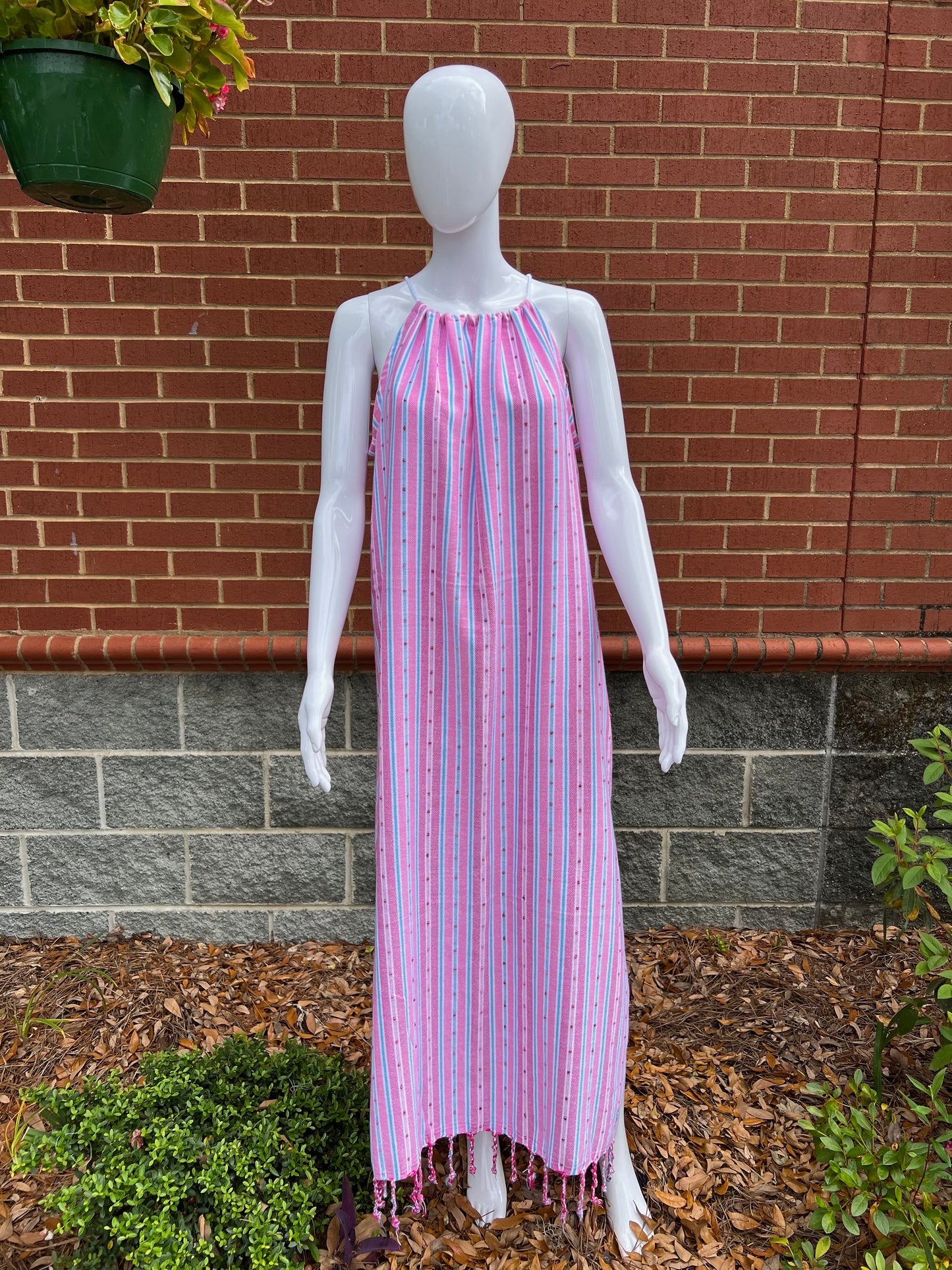 Mannequin wearing pink striped sleeveless maxi sundress with tassels in front of brick wall 