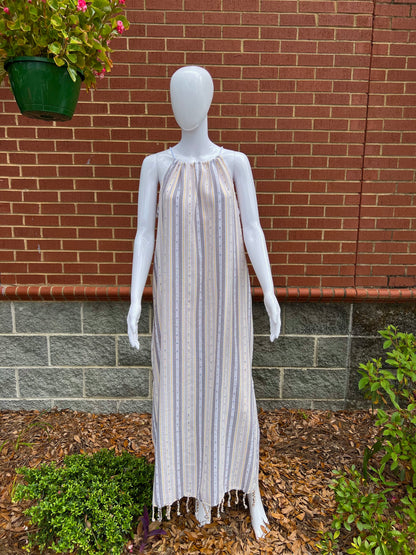 Mannequin wearing tan striped sleeveless maxi sundress with tassels in front of brick wall 