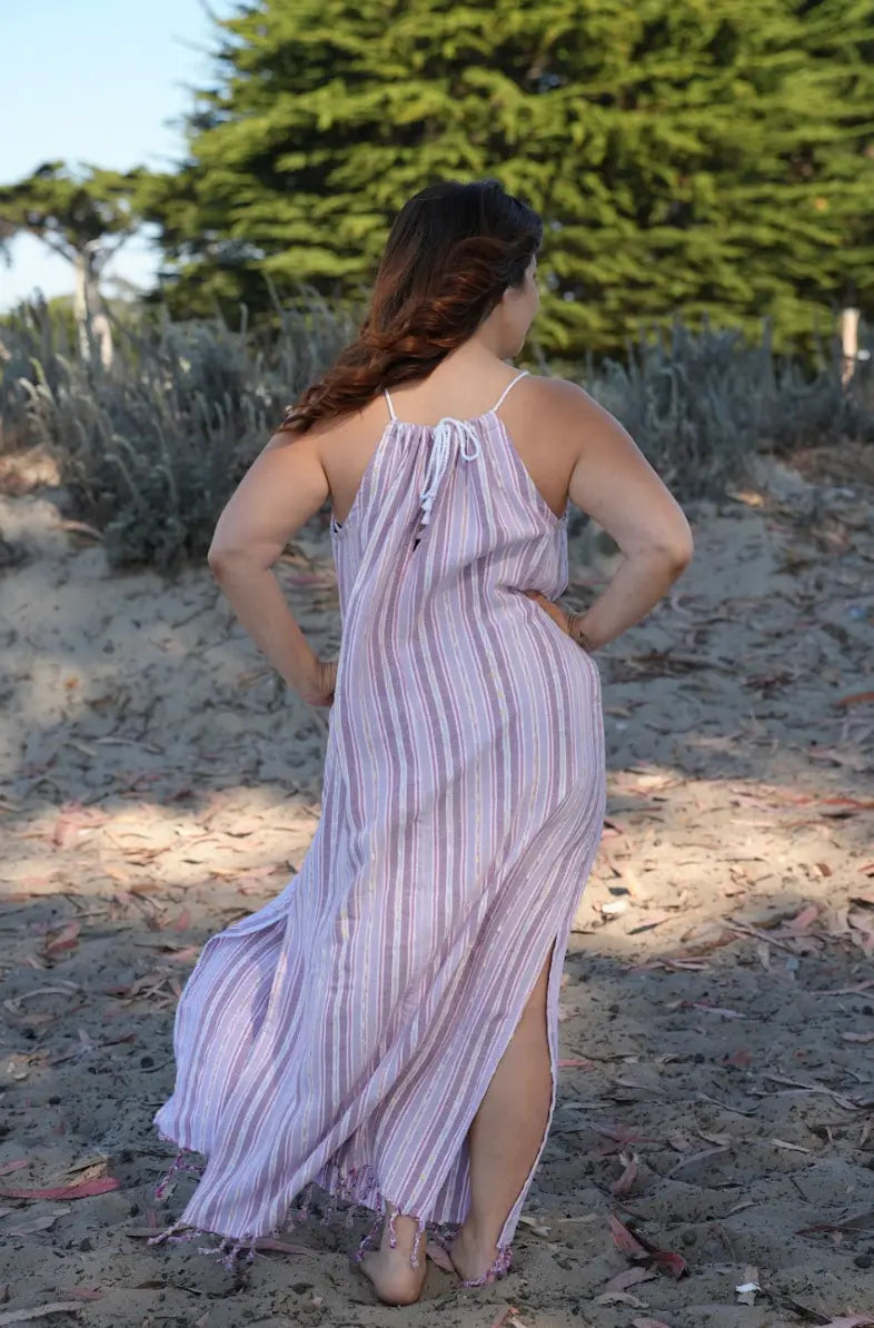 Woman in a purple striped dress standing on a sandy beach with trees in the background