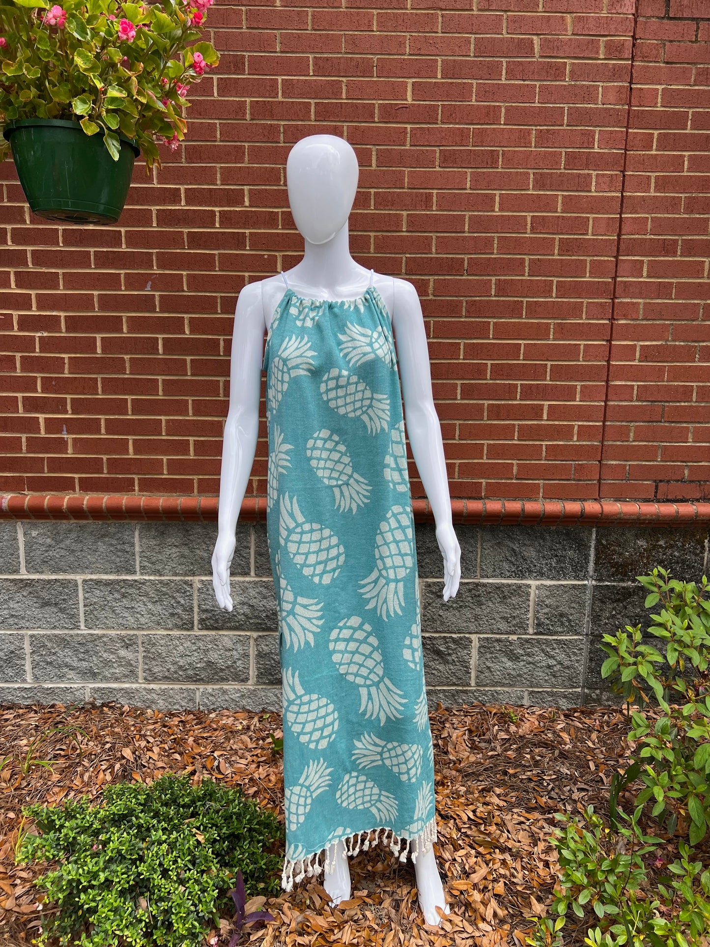 Mannequin wearing green pineapple print sleeveless maxi sundress with tassels in front of brick wall 