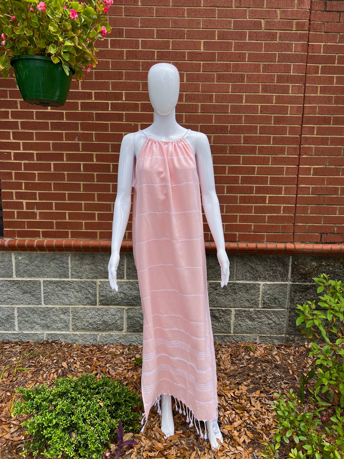 Mannequin wearing peach striped sleeveless maxi sundress with tassels in front of brick wall 