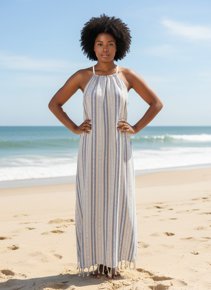 Woman in a tan striped dress standing on a beach with ocean in the background