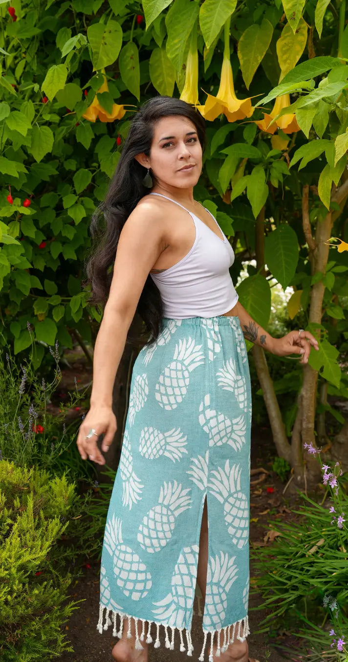 A woman wearing a green pineapple print maxi skirt with tassels, paired with a white top, standing outdoors.