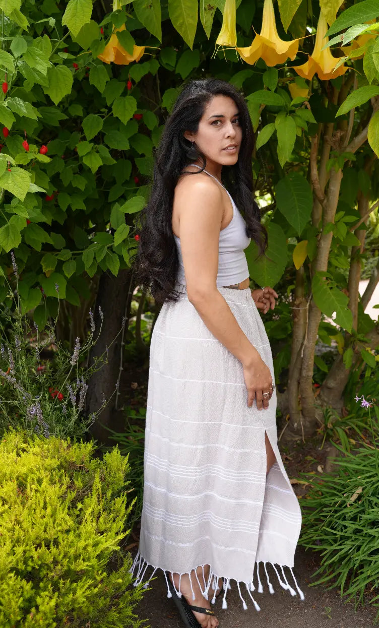 A woman wearing a brown striped midi skirt with tassels, paired with a white top, standing outdoors.