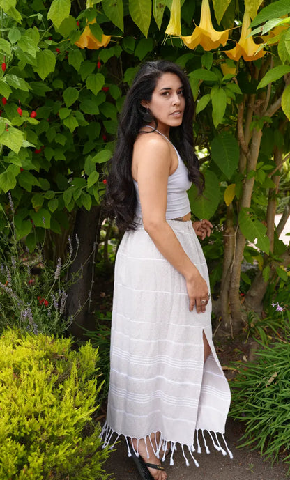 A woman wearing a brown striped midi skirt with tassels, paired with a white top, standing outdoors.