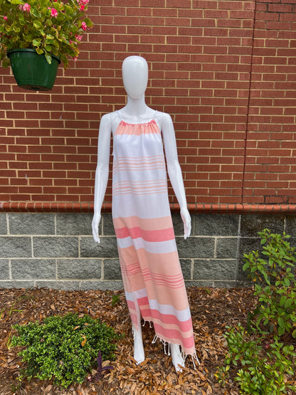 Mannequin wearing peach, red and white striped sleeveless maxi sundress with tassels in front of brick wall 
