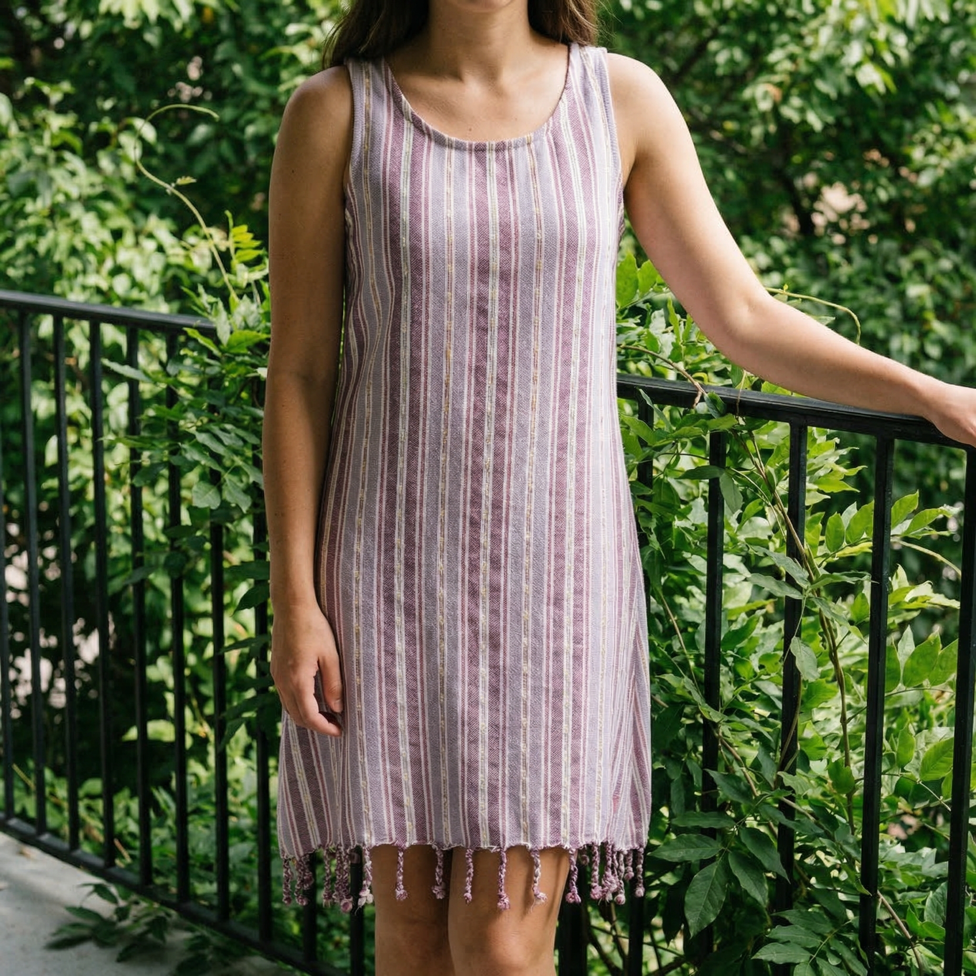 Woman wearing a purple striped dress with tassels standing outdoors with greenery in the background