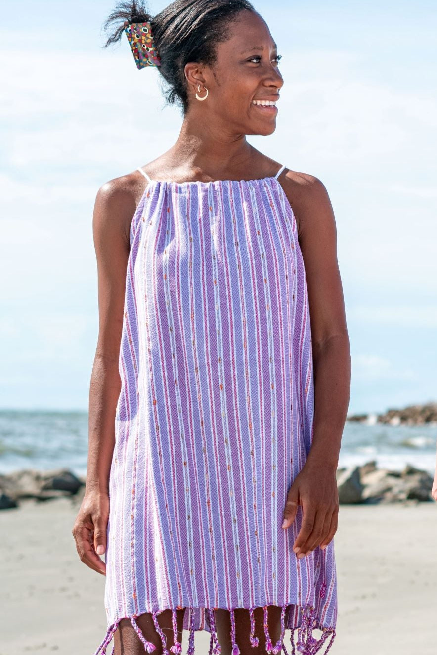 A woman standing on a beach wearing a sleeveless, striped red and white mini dress with tassels.