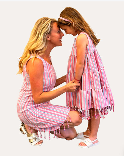 Young girl wearing a three-tiered pink striped sleeveless dress with tassels touching foreheads with a woman in a matching dress