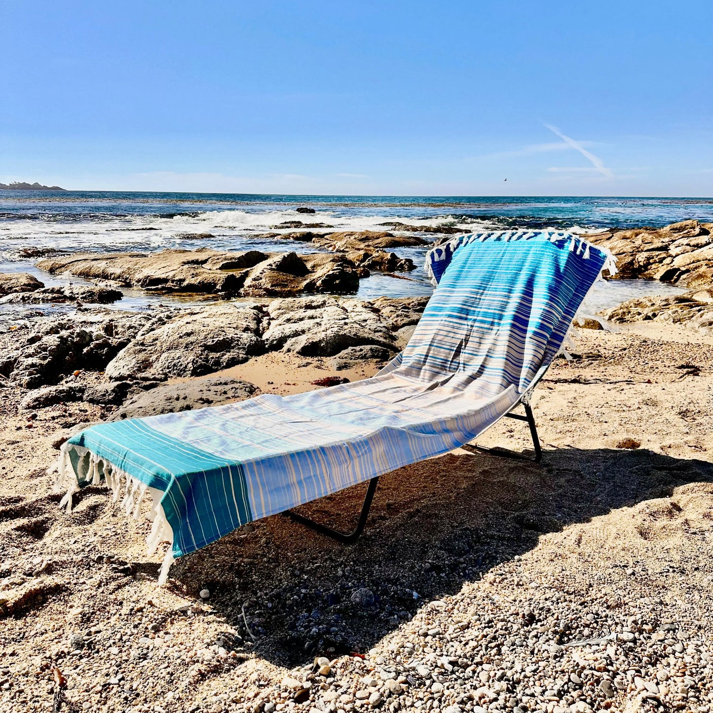 Blue striped towel draped over a lounge chair on a rocky beach.
