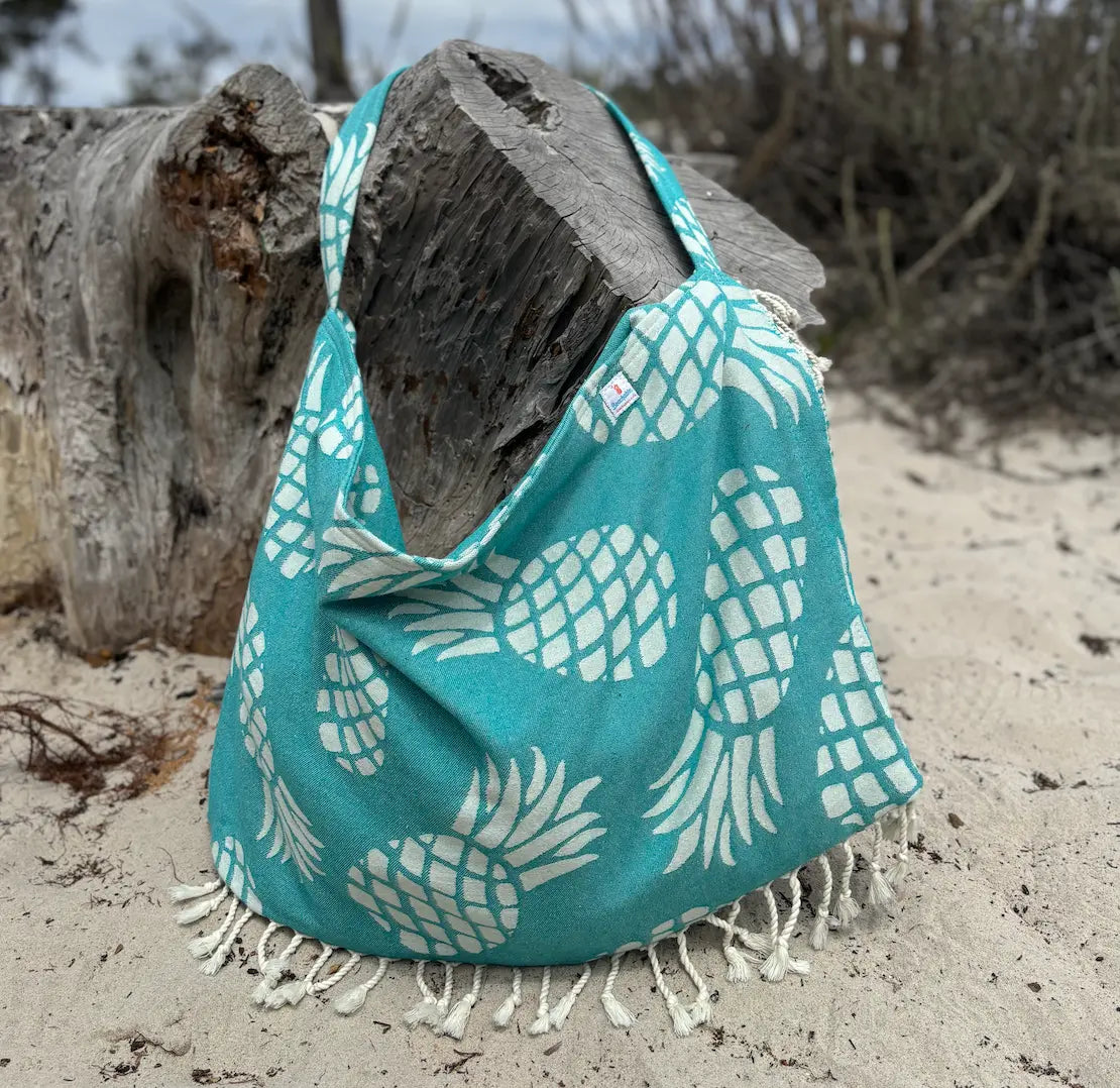 Green bag with white pineapple pattern on a sandy beach