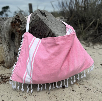 Pink and white beach bag with tassels on a sandy background