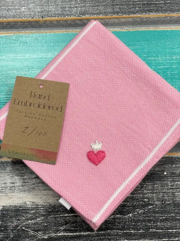 Pink hand-embroidered napkin with a heart design on a wooden surface