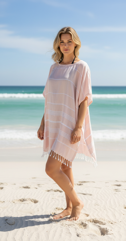 Woman standing on a beach wearing a peach cover-up with white stripes.