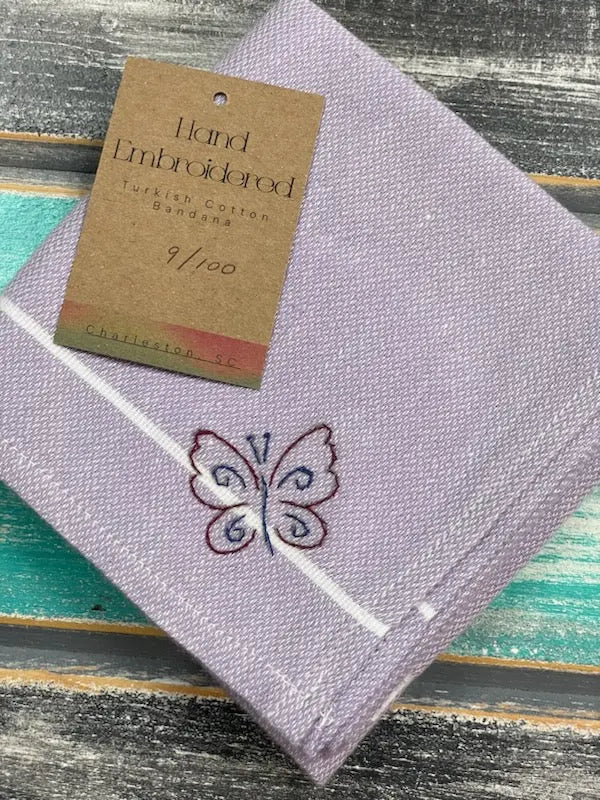 Purple embroidered bandana with a butterfly design on a wooden surface