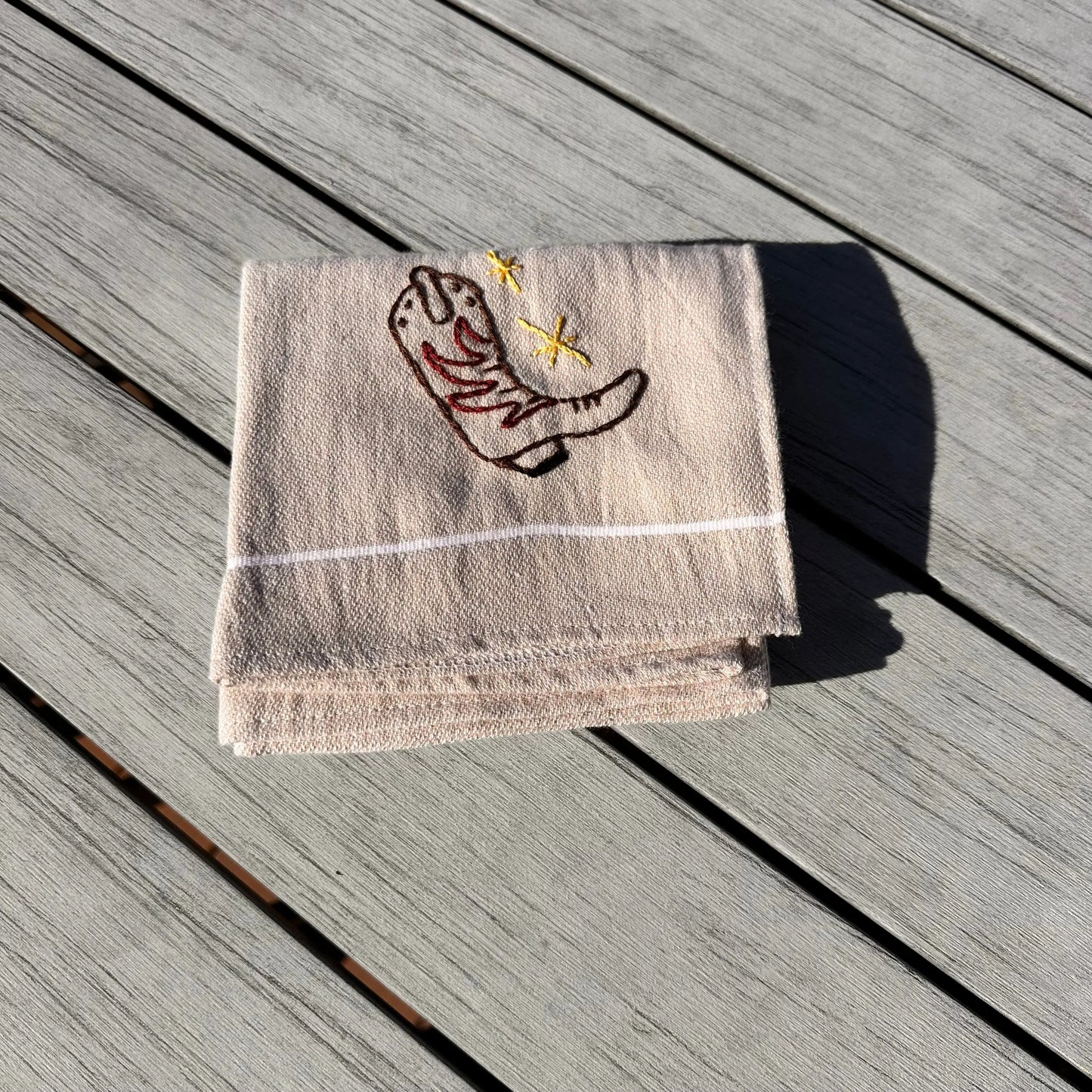 Brown towel with embroidered cowboy boot design on a wooden surface