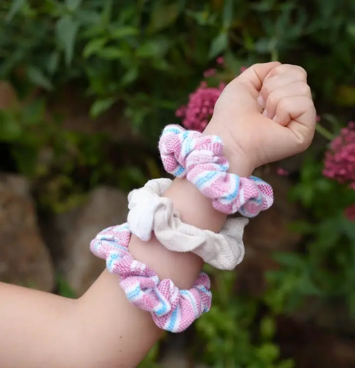 Hand wearing three colorful scrunchies with a blurred natural background
