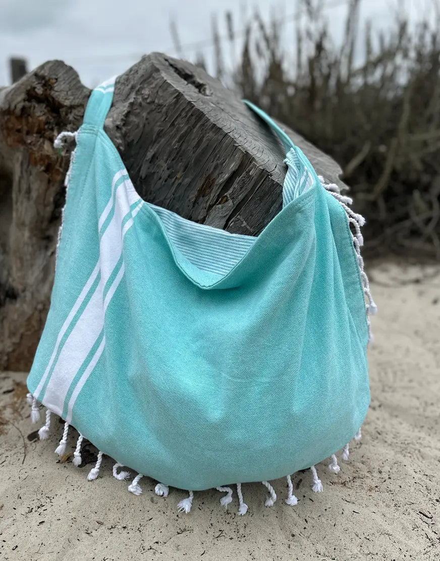 Teal green beach bag with white stripes and tassels on a sandy background