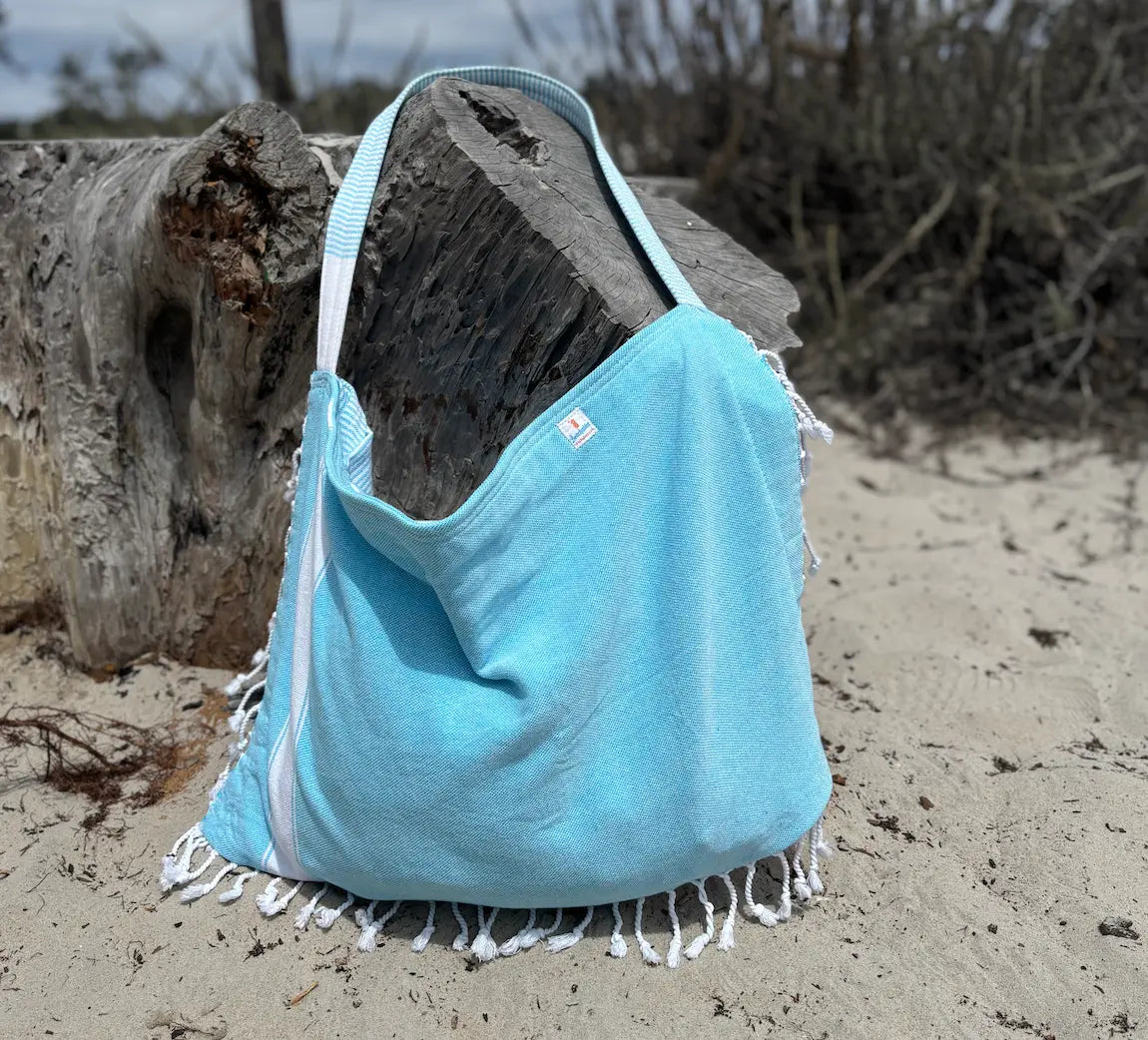 Light blue beach bag with white fringe on a sandy background