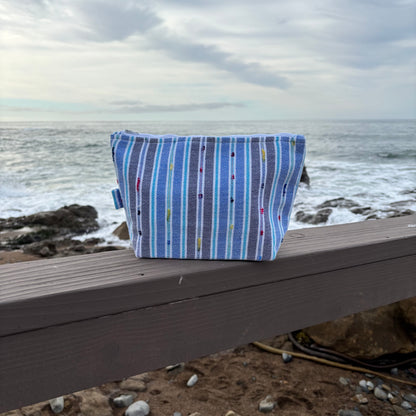 Large sized  blue striped makeup bag placed on a surface with a coastal background.
