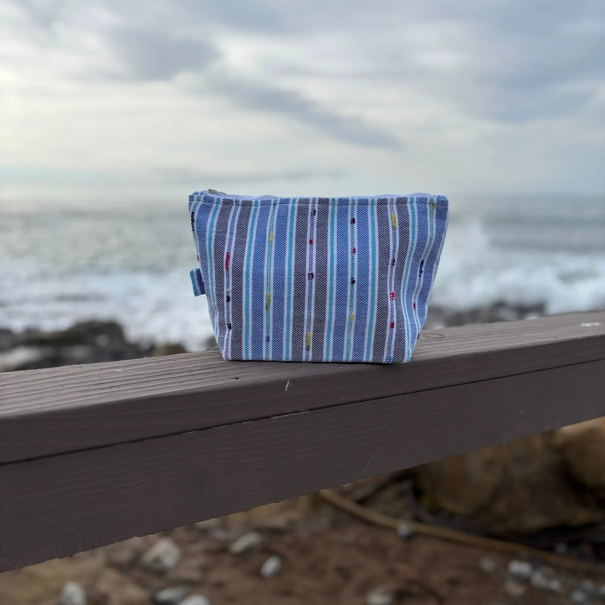 Blue striped fabric pouch on a wooden surface with a beach background